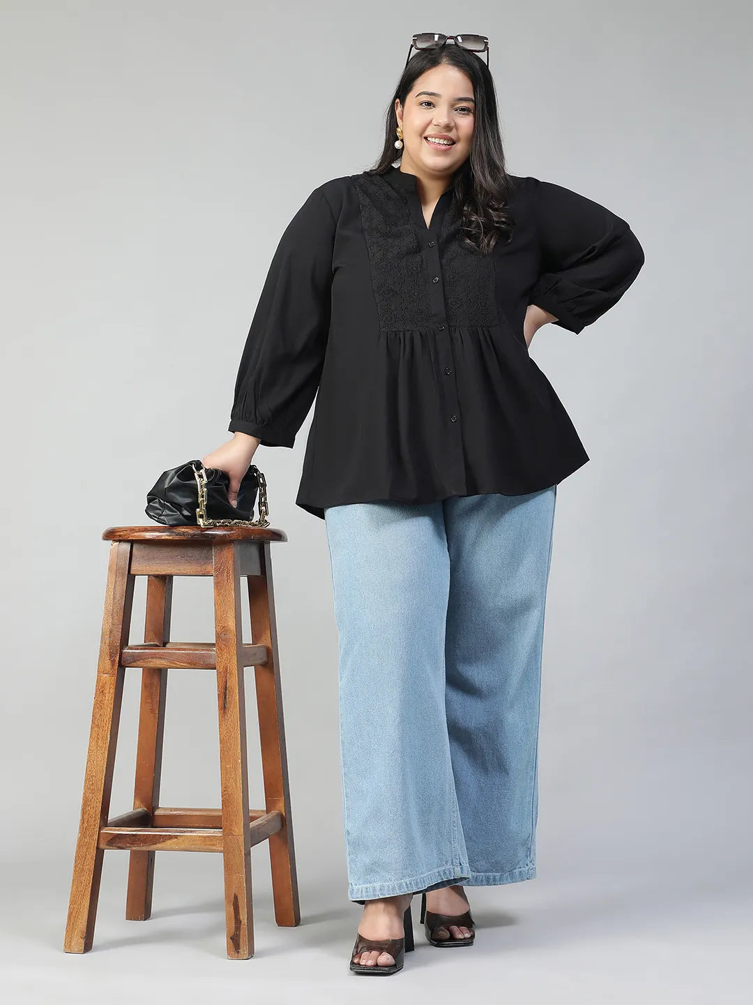 A woman with long dark hair is smiling and posing for the camera, wearing a black blouse with lace detailing and puffed sleeves.