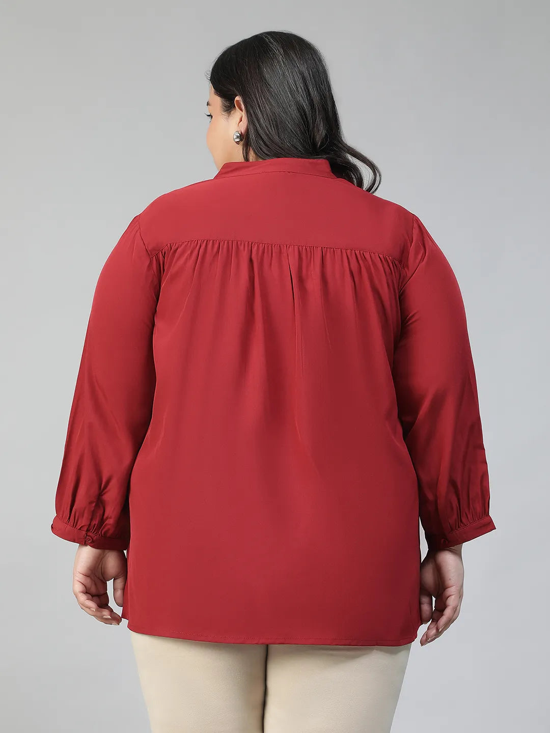 A smiling woman wearing a red blouse with a lace pattern and a high collar, posing confidently with her hand on her hip.
