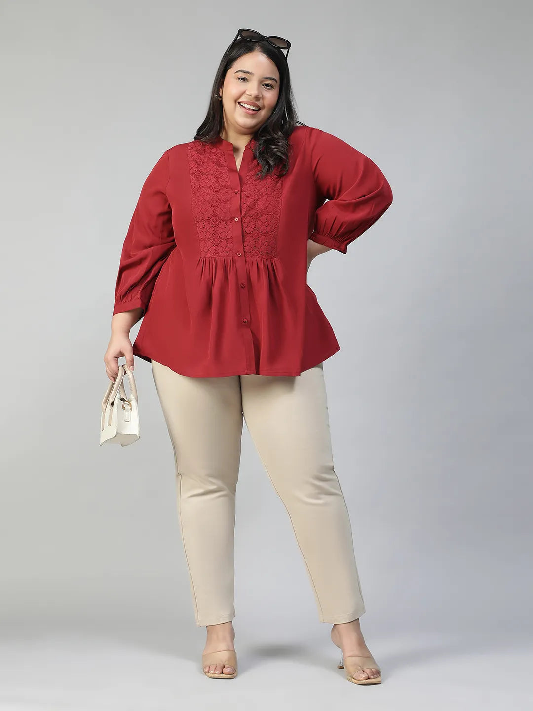 A smiling woman wearing a red blouse with a lace pattern and a high collar, posing confidently with her hand on her hip.