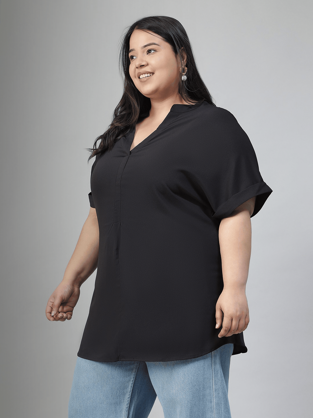 A woman with long dark hair is smiling and wearing a black top and blue jeans.