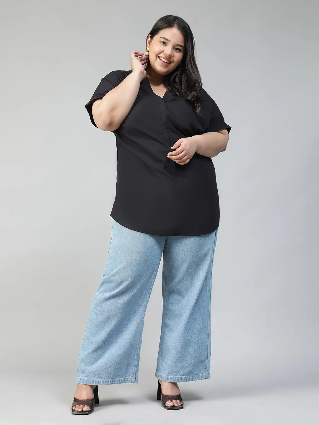 A woman with long dark hair is smiling and wearing a black top and blue jeans.