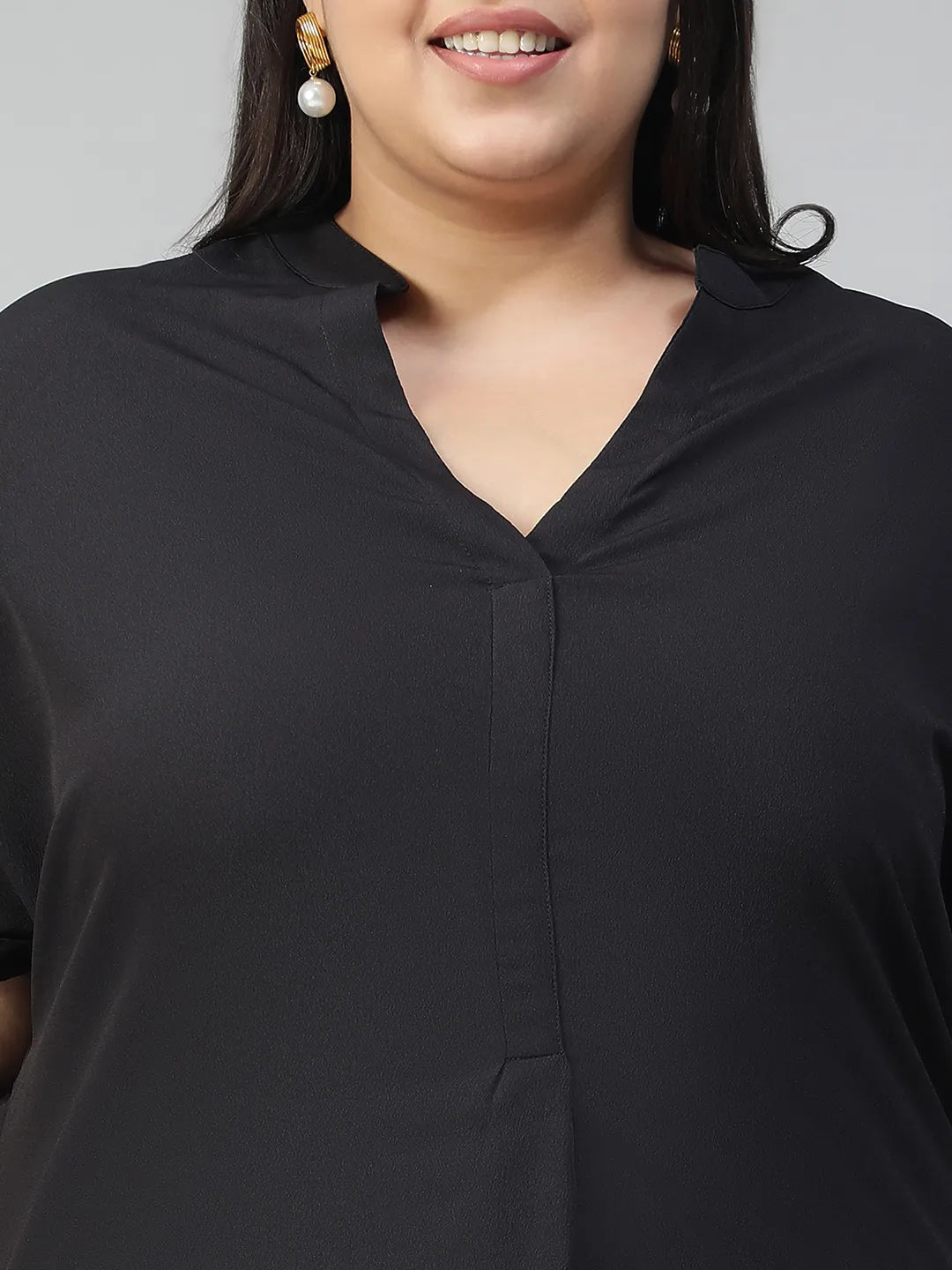 A woman with long dark hair is smiling and wearing a black top and blue jeans.