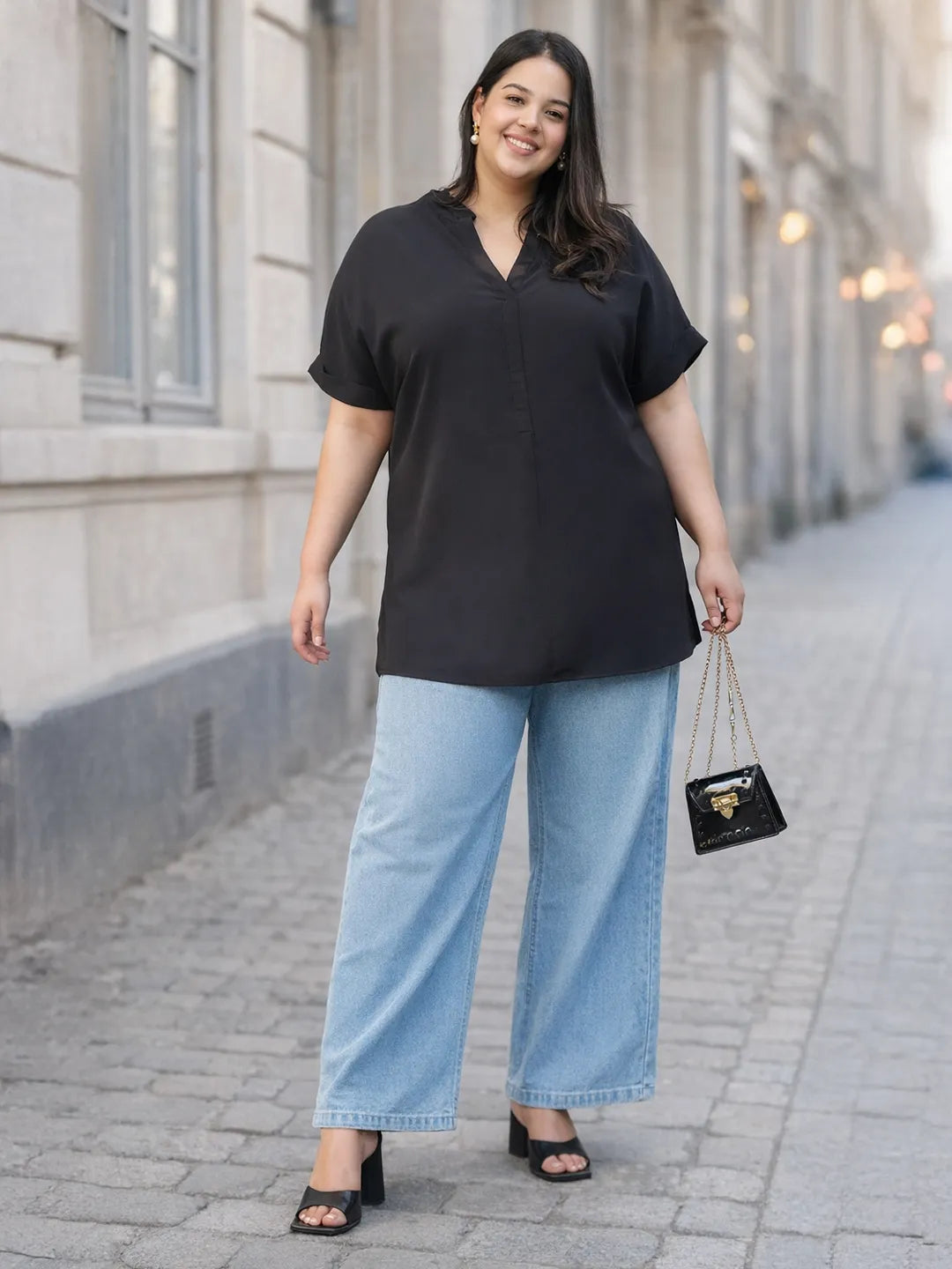A woman with long dark hair is smiling and wearing a black top and blue jeans.