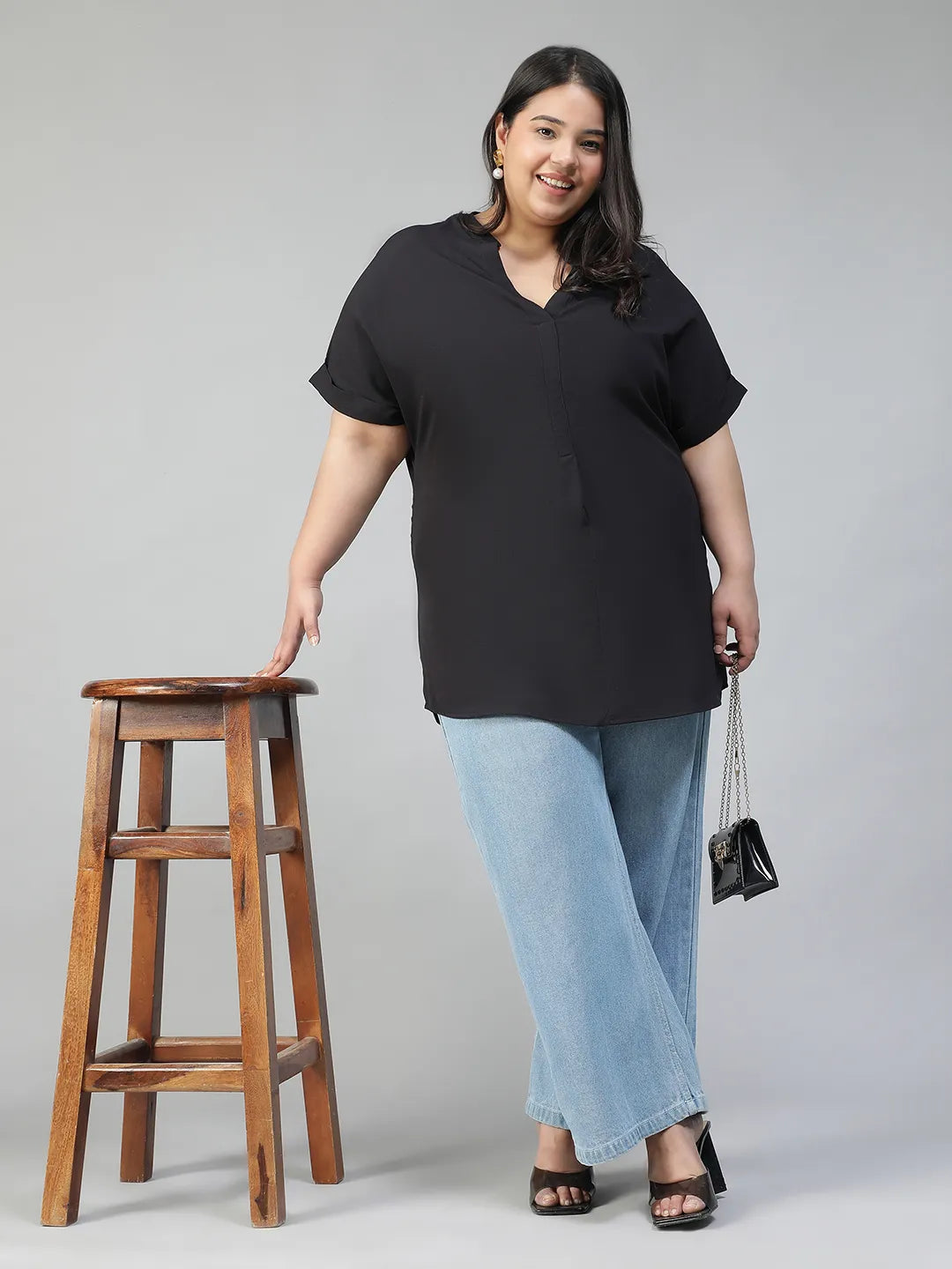 A woman with long dark hair is smiling and wearing a black top and blue jeans.