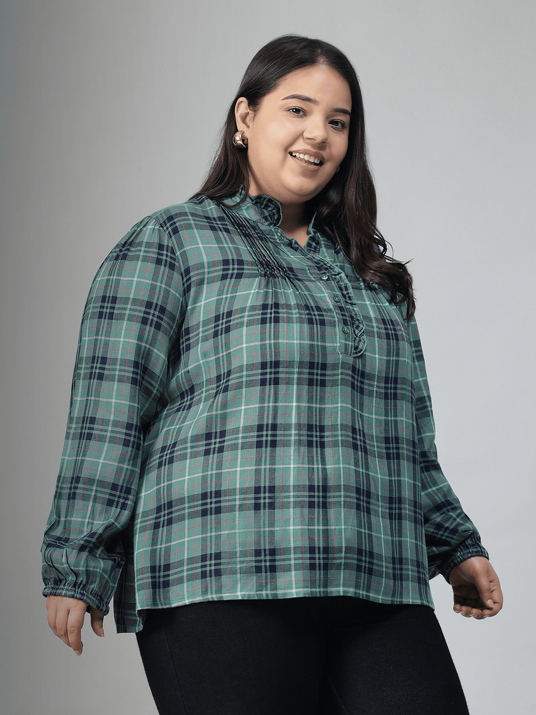A smiling woman wearing a green and blue plaid shirt with long sleeves, posing for a portrait.