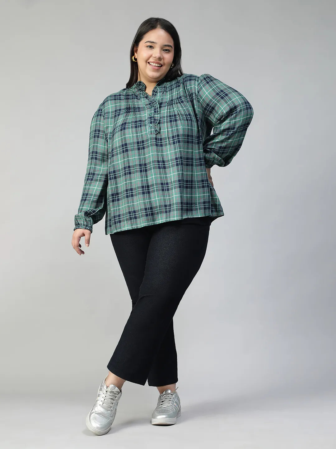 A smiling woman wearing a green and blue plaid shirt with long sleeves, posing for a portrait.