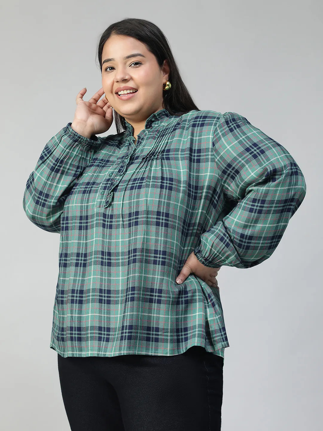 A smiling woman wearing a green and blue plaid shirt with long sleeves, posing for a portrait.