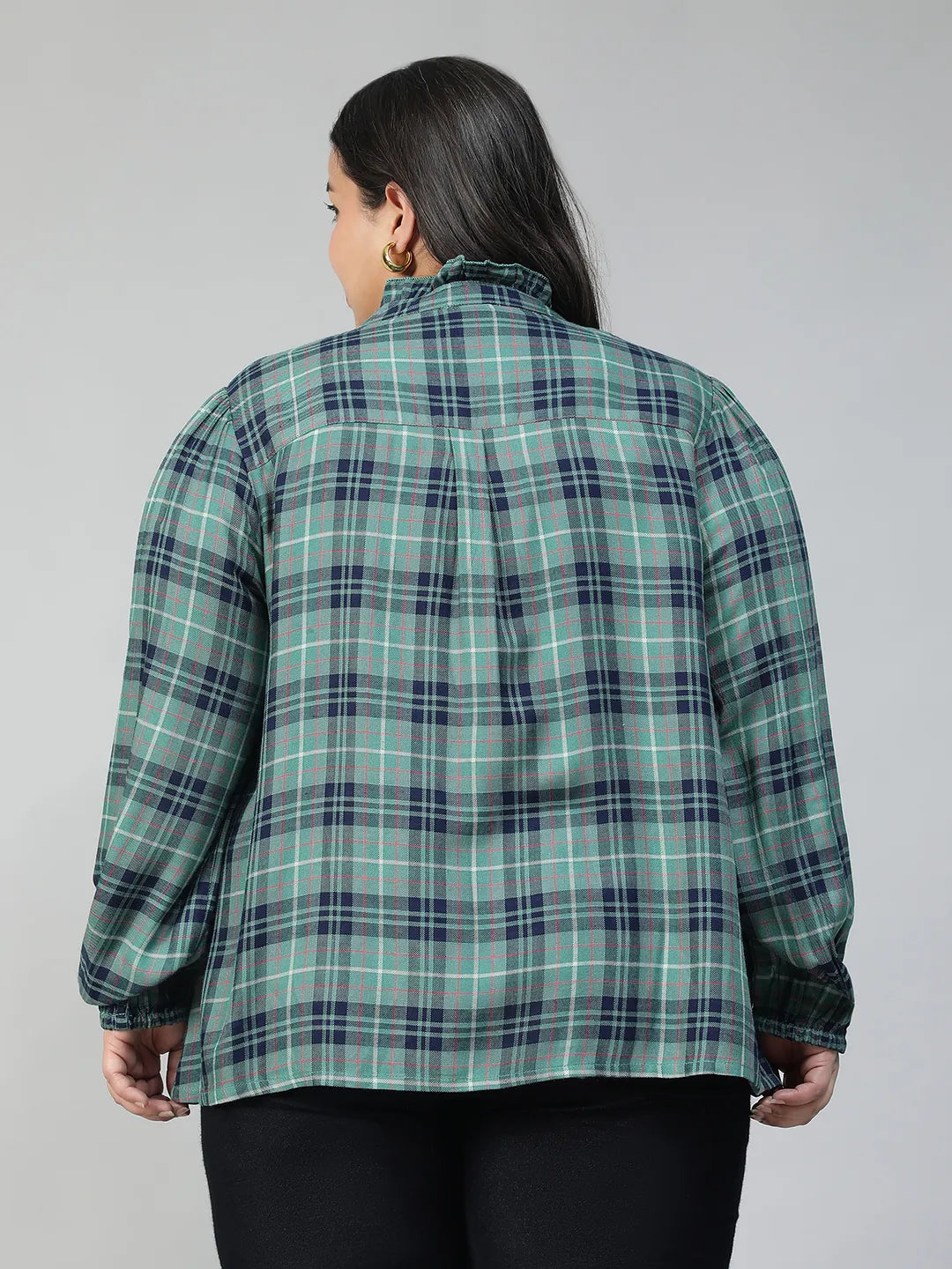 A smiling woman wearing a green and blue plaid shirt with long sleeves, posing for a portrait.