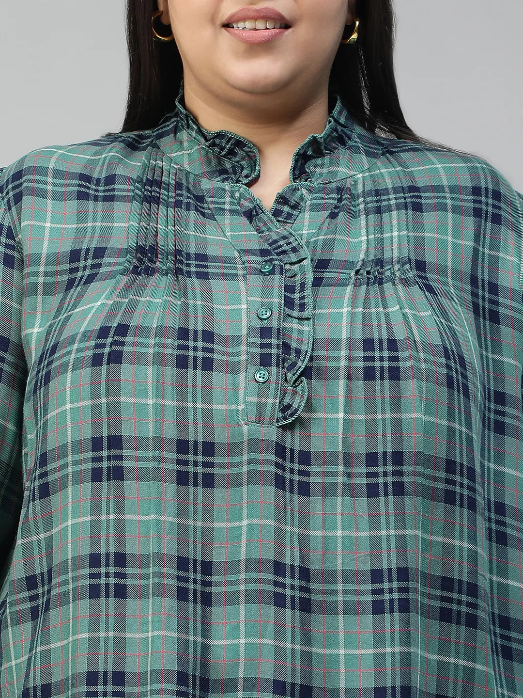 A smiling woman wearing a green and blue plaid shirt with long sleeves, posing for a portrait.