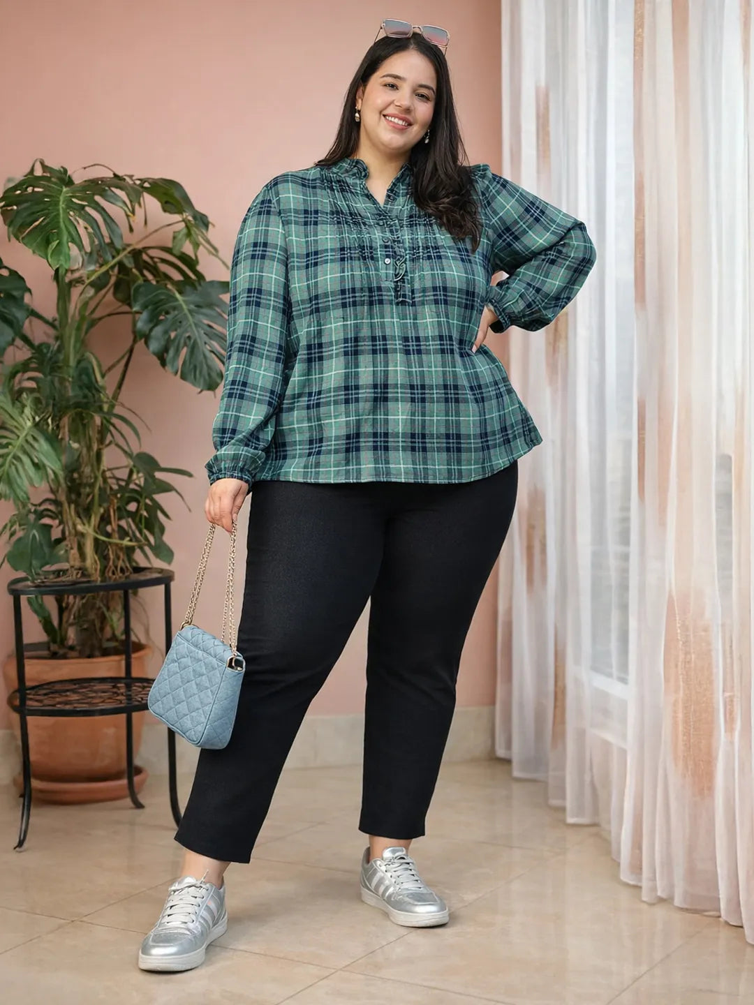 A smiling woman wearing a green and blue plaid shirt with long sleeves, posing for a portrait.
