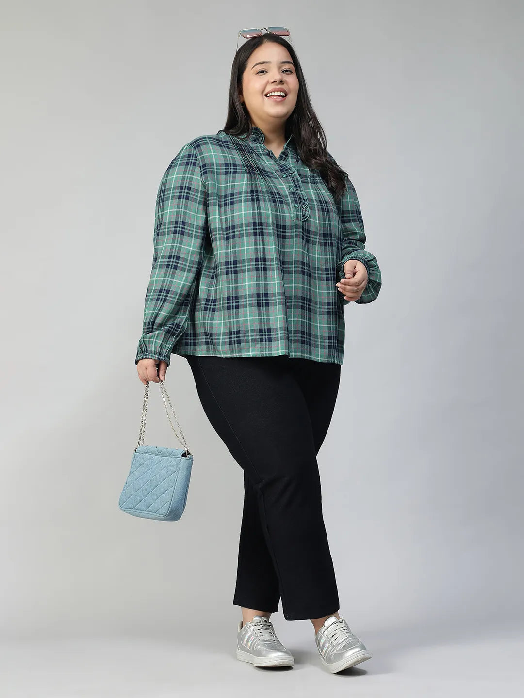 A smiling woman wearing a green and blue plaid shirt with long sleeves, posing for a portrait.