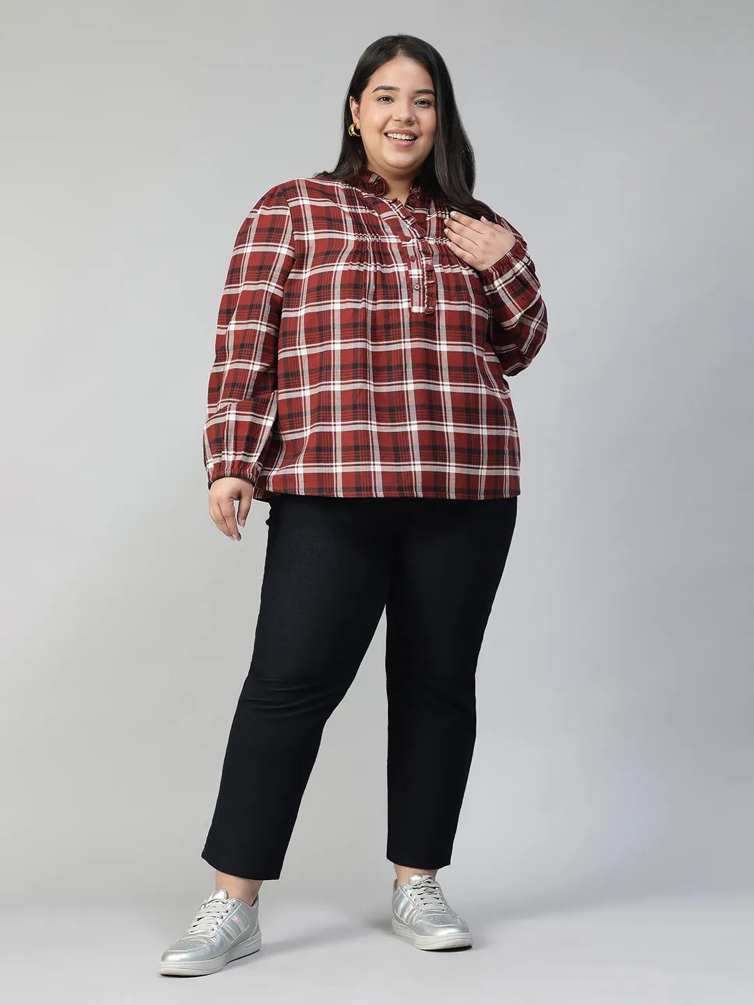 A woman with long dark hair is smiling and posing for the camera, wearing a red and white plaid shirt.