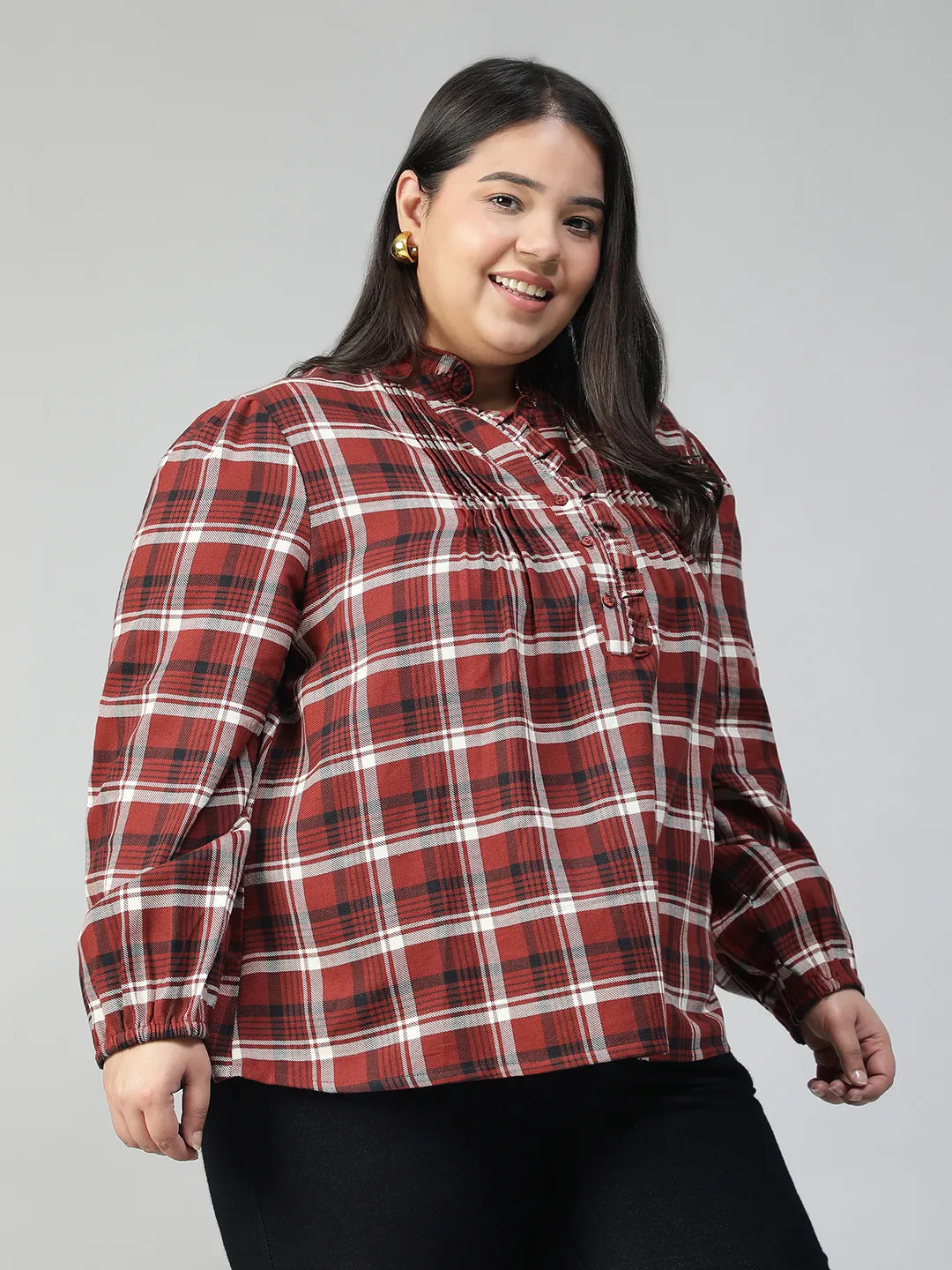 A woman with long dark hair is smiling and posing for the camera, wearing a red and white plaid shirt.