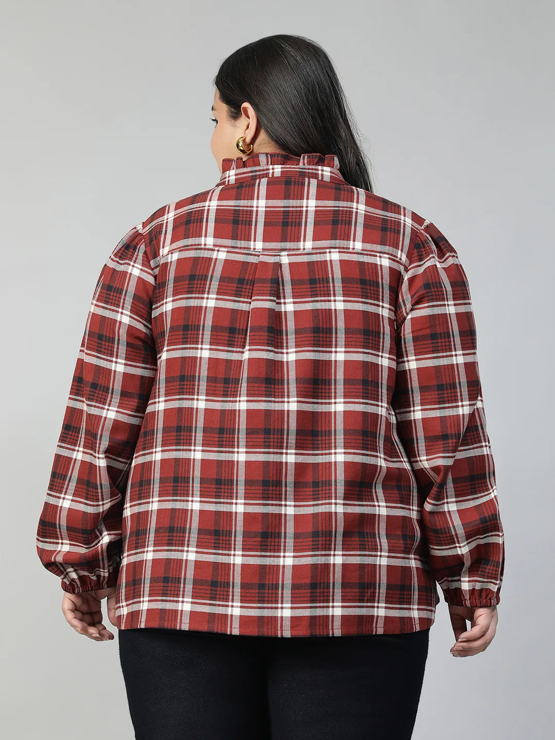 A woman with long dark hair is smiling and posing for the camera, wearing a red and white plaid shirt.