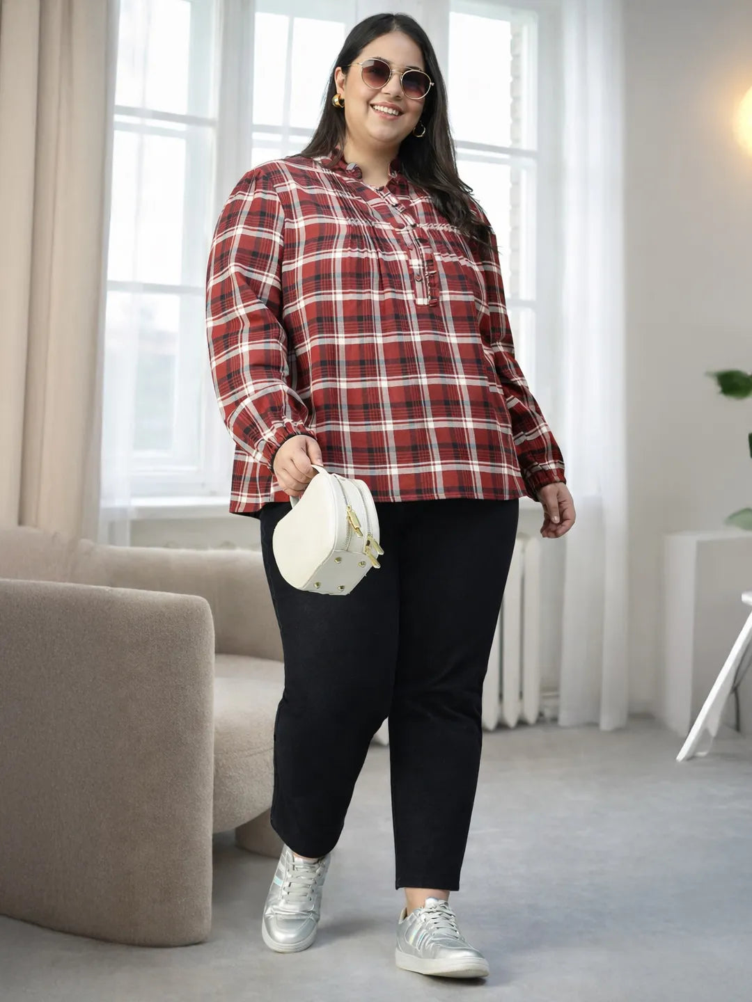 A woman with long dark hair is smiling and posing for the camera, wearing a red and white plaid shirt.