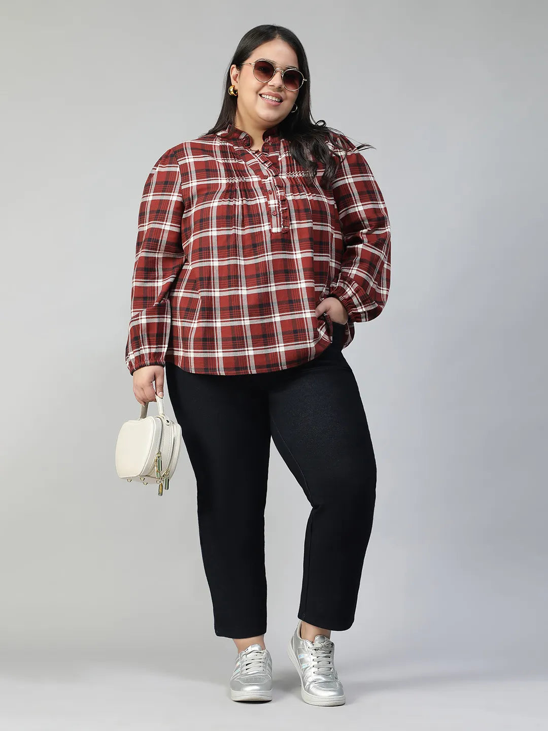 A woman with long dark hair is smiling and posing for the camera, wearing a red and white plaid shirt.