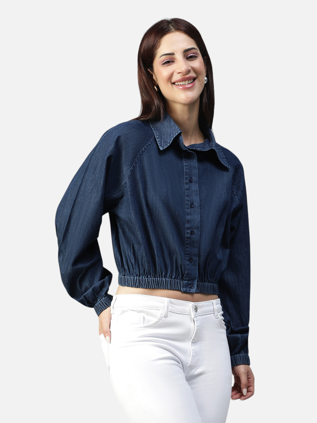 Woman wearing a blue cropped denim shirt and white pants, smiling, front view
