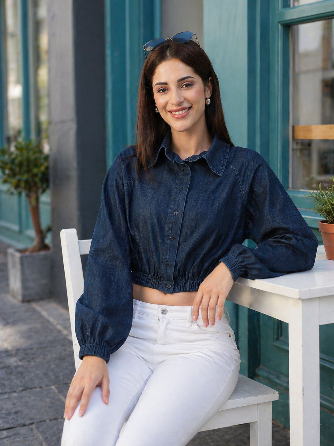 Woman wearing a blue cropped denim shirt and white high-waisted pants sitting outside