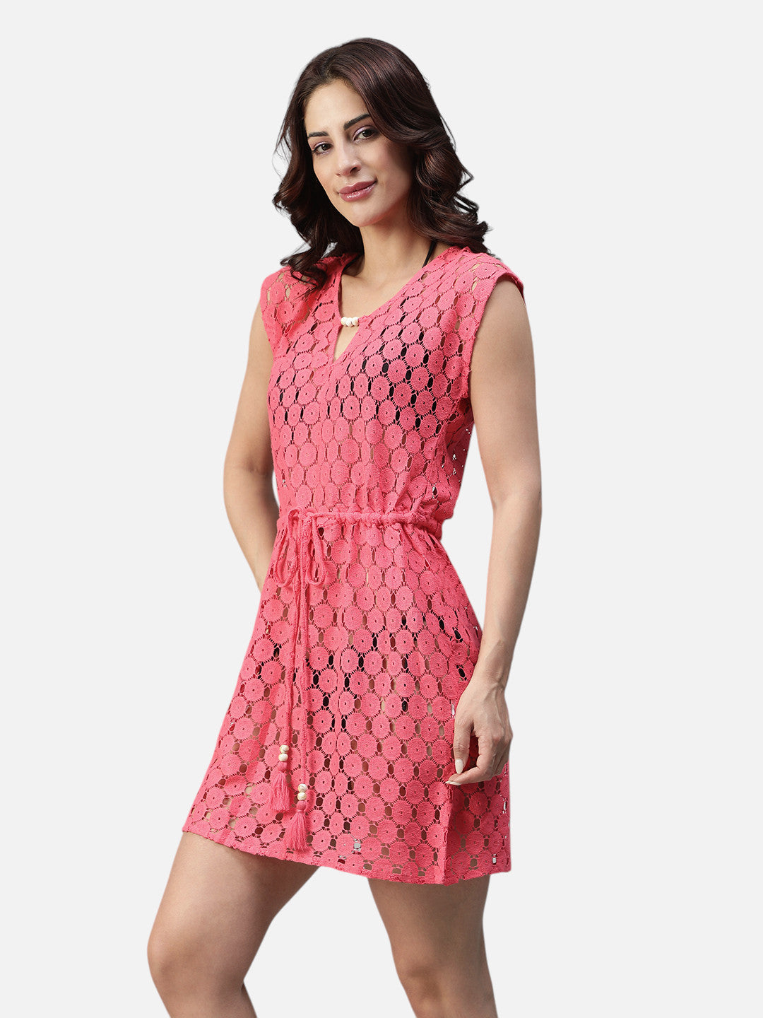 Woman wearing a sleeveless pink eyelet short dress with tie waist, posing against white background