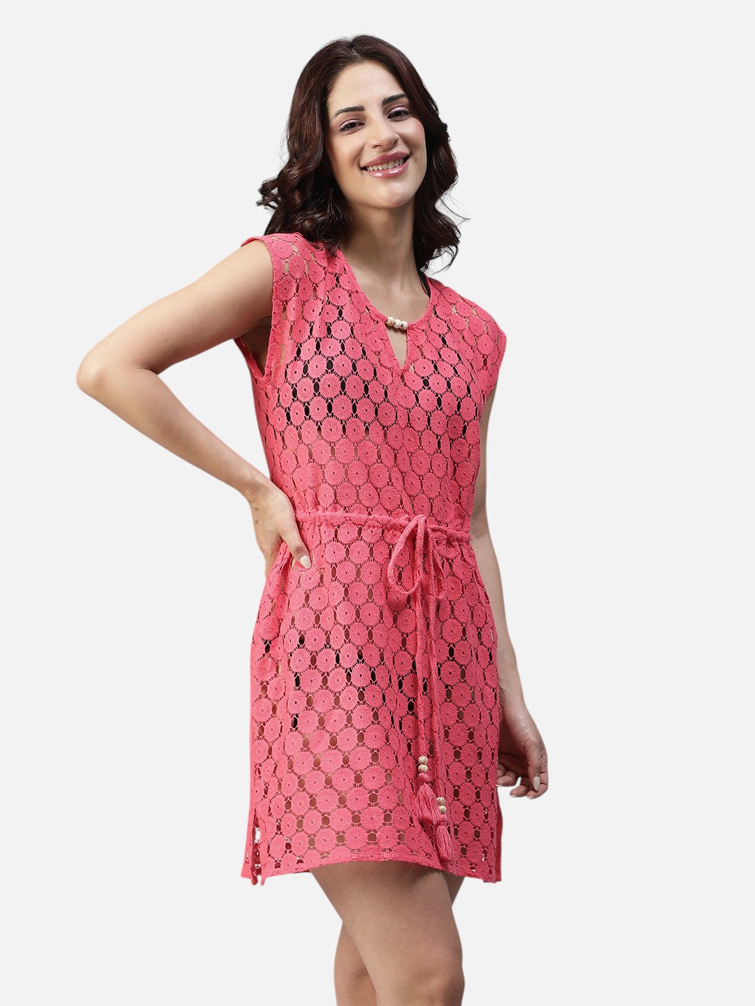 Woman wearing a pink crochet short dress with tie waist and cap sleeves, smiling