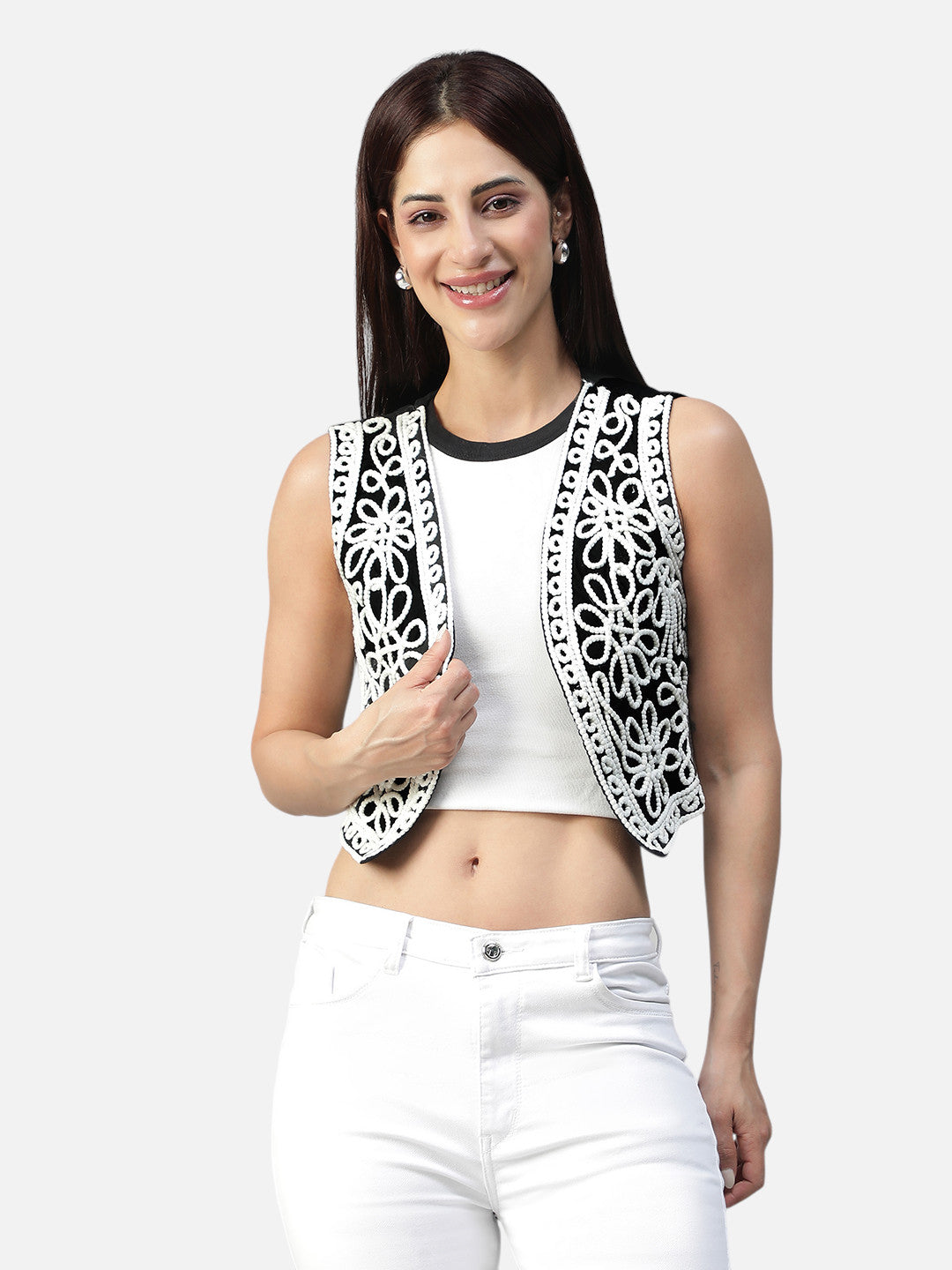 Woman in white crop top, white jeans, and black embroidered sleeveless vest