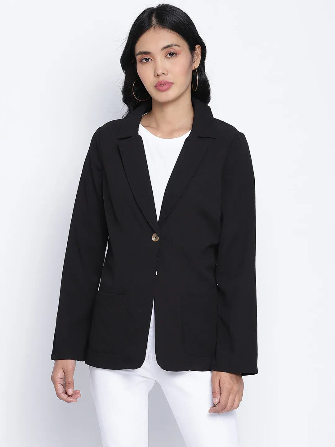 A woman wearing a black blazer, white pants, and white heels, with sunglasses on her head, posing against a white background.