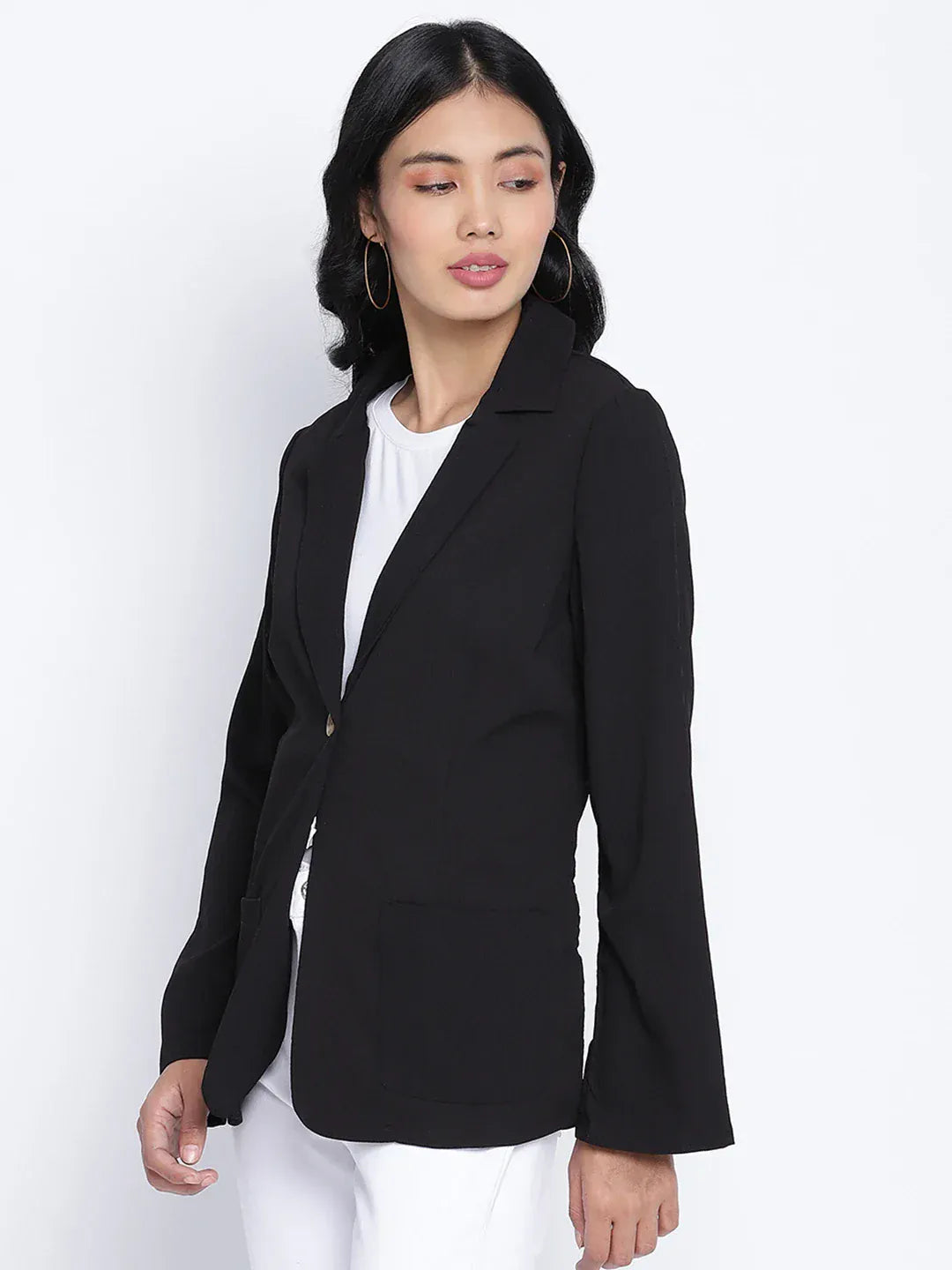 A woman wearing a black blazer, white pants, and white heels, with sunglasses on her head, posing against a white background.