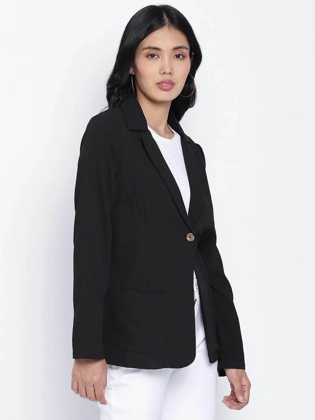 A woman wearing a black blazer, white pants, and white heels, with sunglasses on her head, posing against a white background.