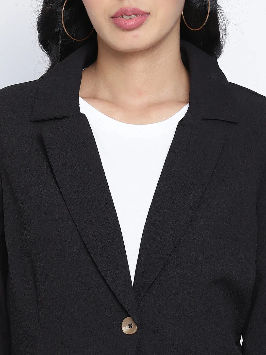 A woman wearing a black blazer, white pants, and white heels, with sunglasses on her head, posing against a white background.