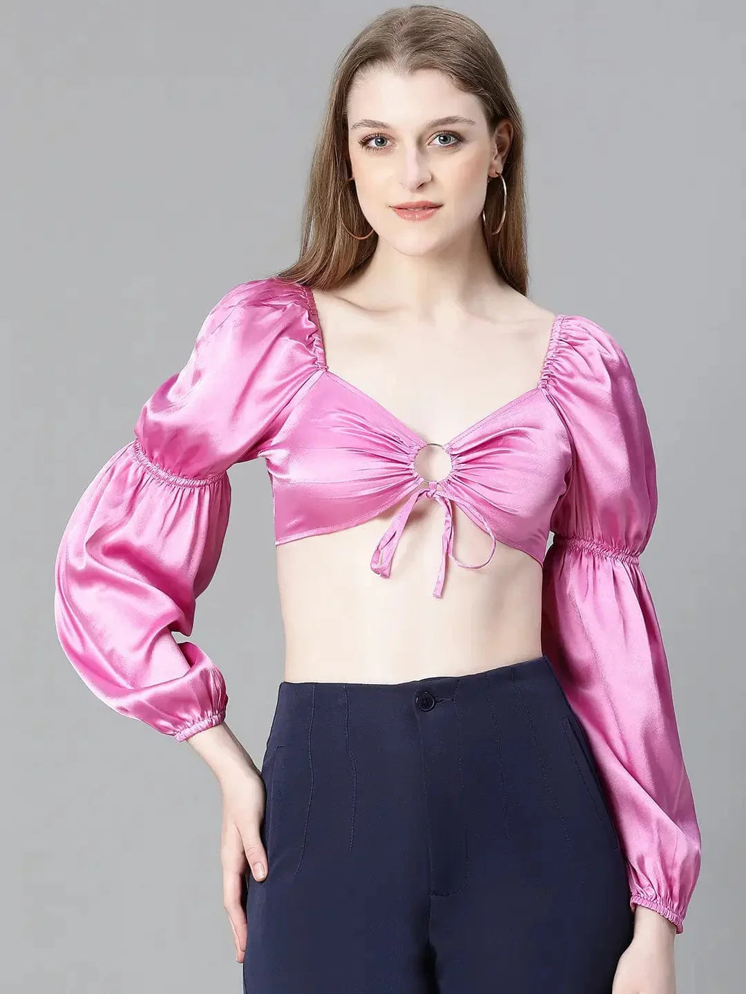 A woman with long brown hair wearing a pink one-shoulder top and blue pants, smiling at the camera.