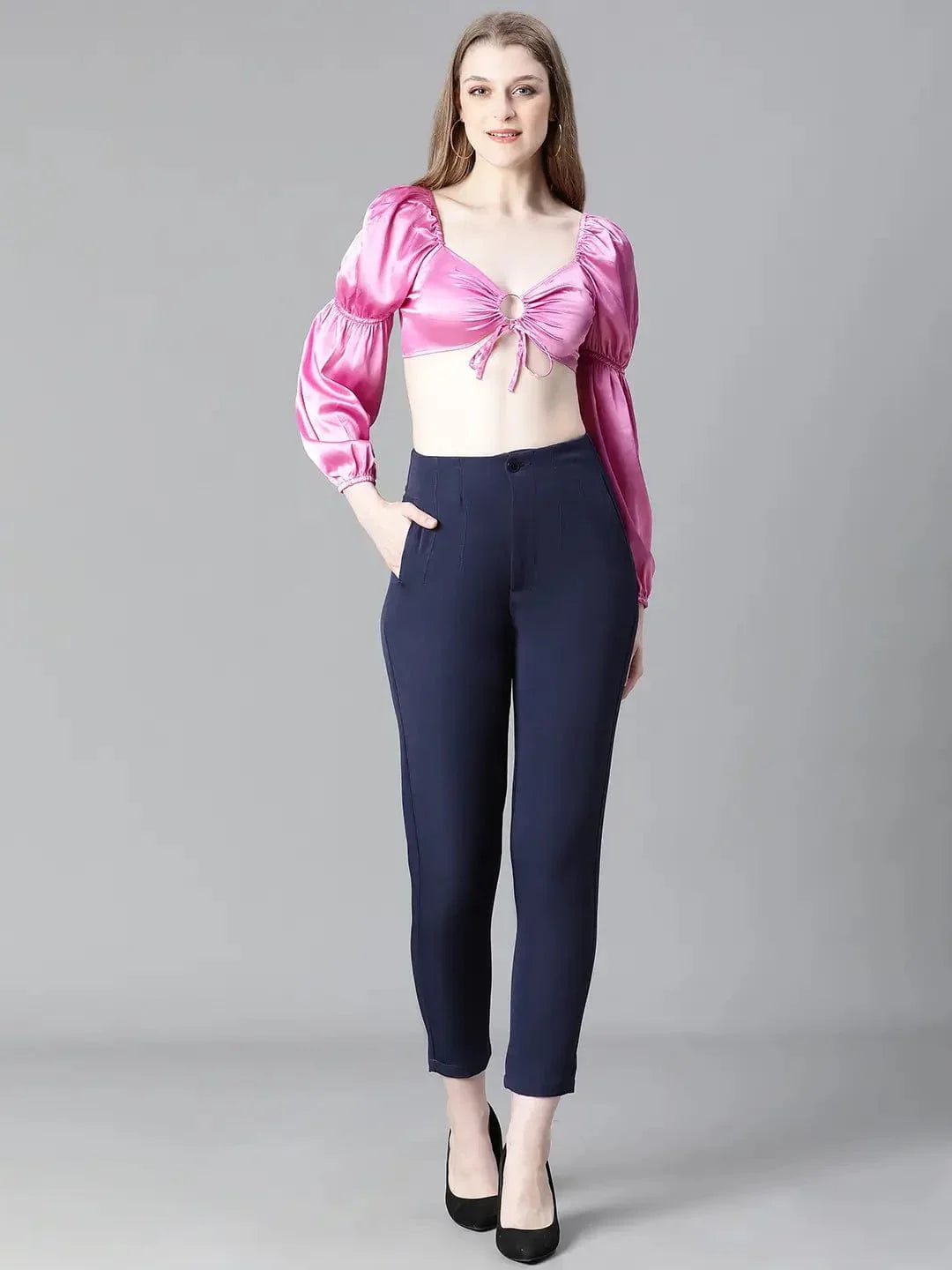 A woman with long brown hair wearing a pink one-shoulder top and blue pants, smiling at the camera.