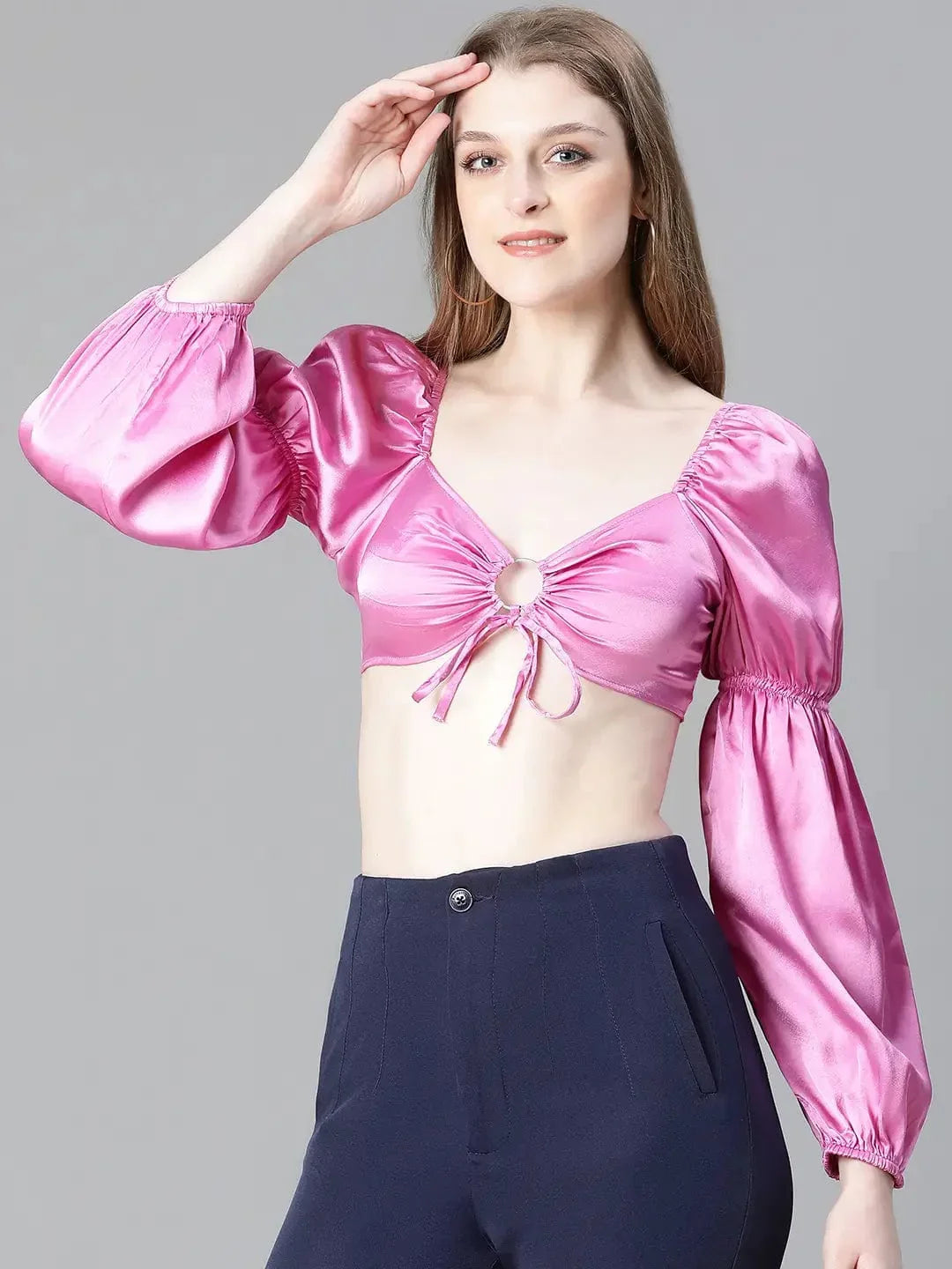 A woman with long brown hair wearing a pink one-shoulder top and blue pants, smiling at the camera.