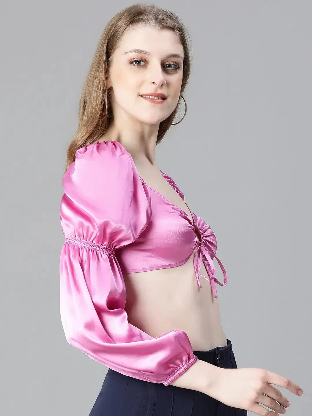 A woman with long brown hair wearing a pink one-shoulder top and blue pants, smiling at the camera.