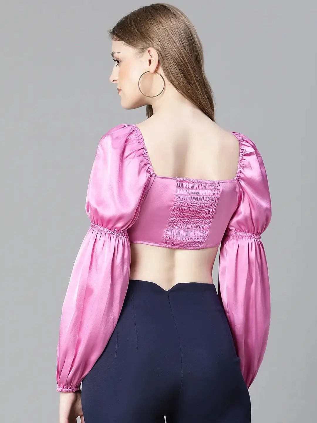 A woman with long brown hair wearing a pink one-shoulder top and blue pants, smiling at the camera.