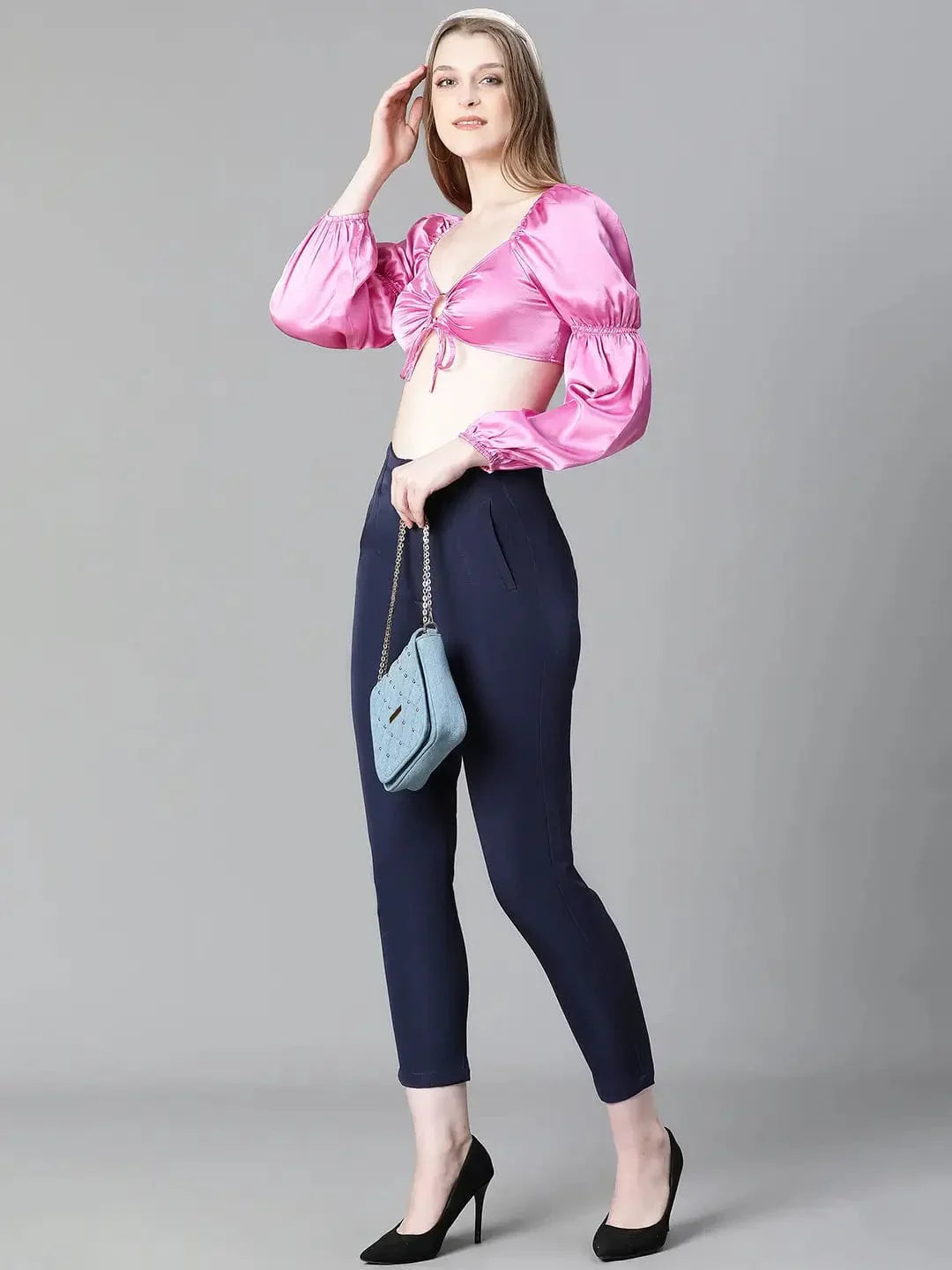 A woman with long brown hair wearing a pink one-shoulder top and blue pants, smiling at the camera.