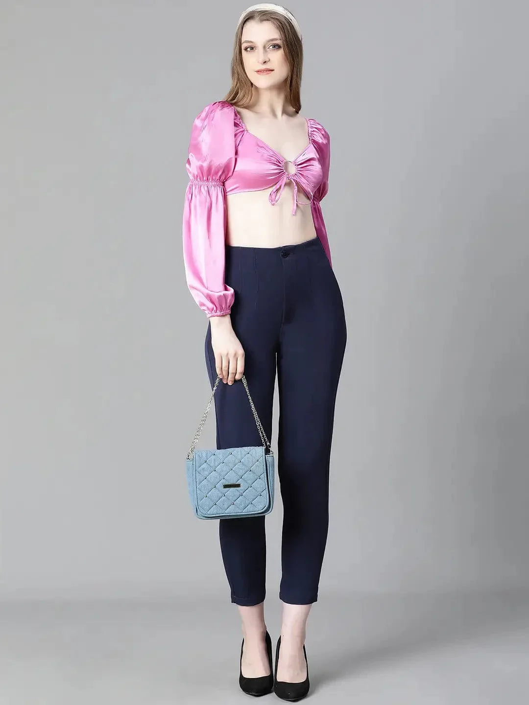 A woman with long brown hair wearing a pink one-shoulder top and blue pants, smiling at the camera.