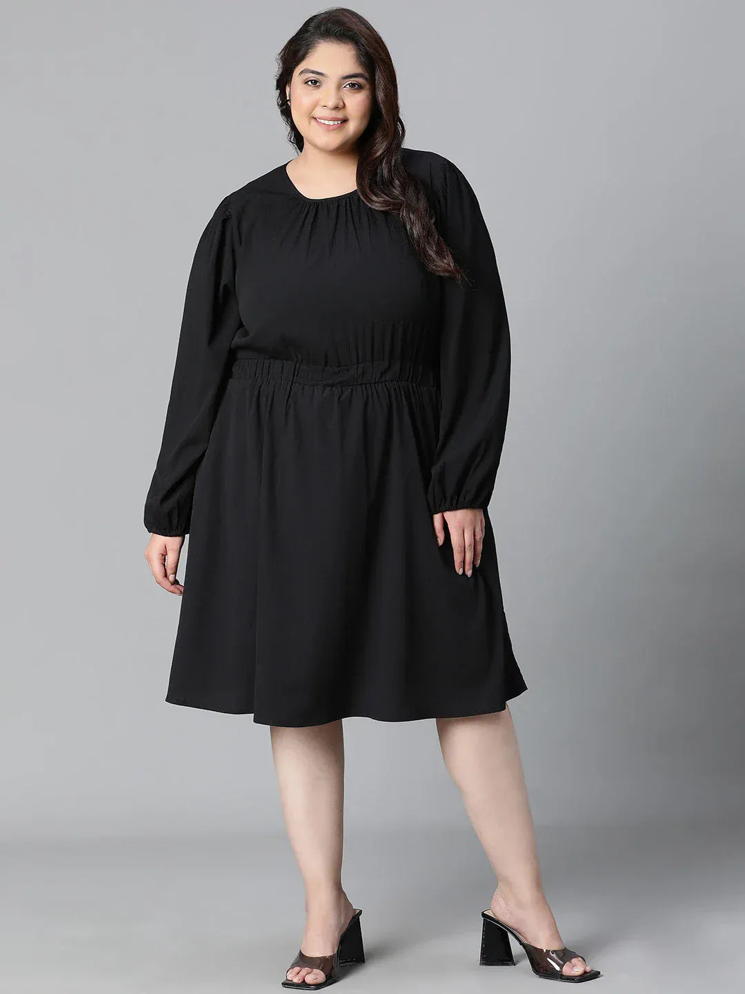 A woman wearing a black dress with long sleeves and a ruched waist, smiling at the camera.