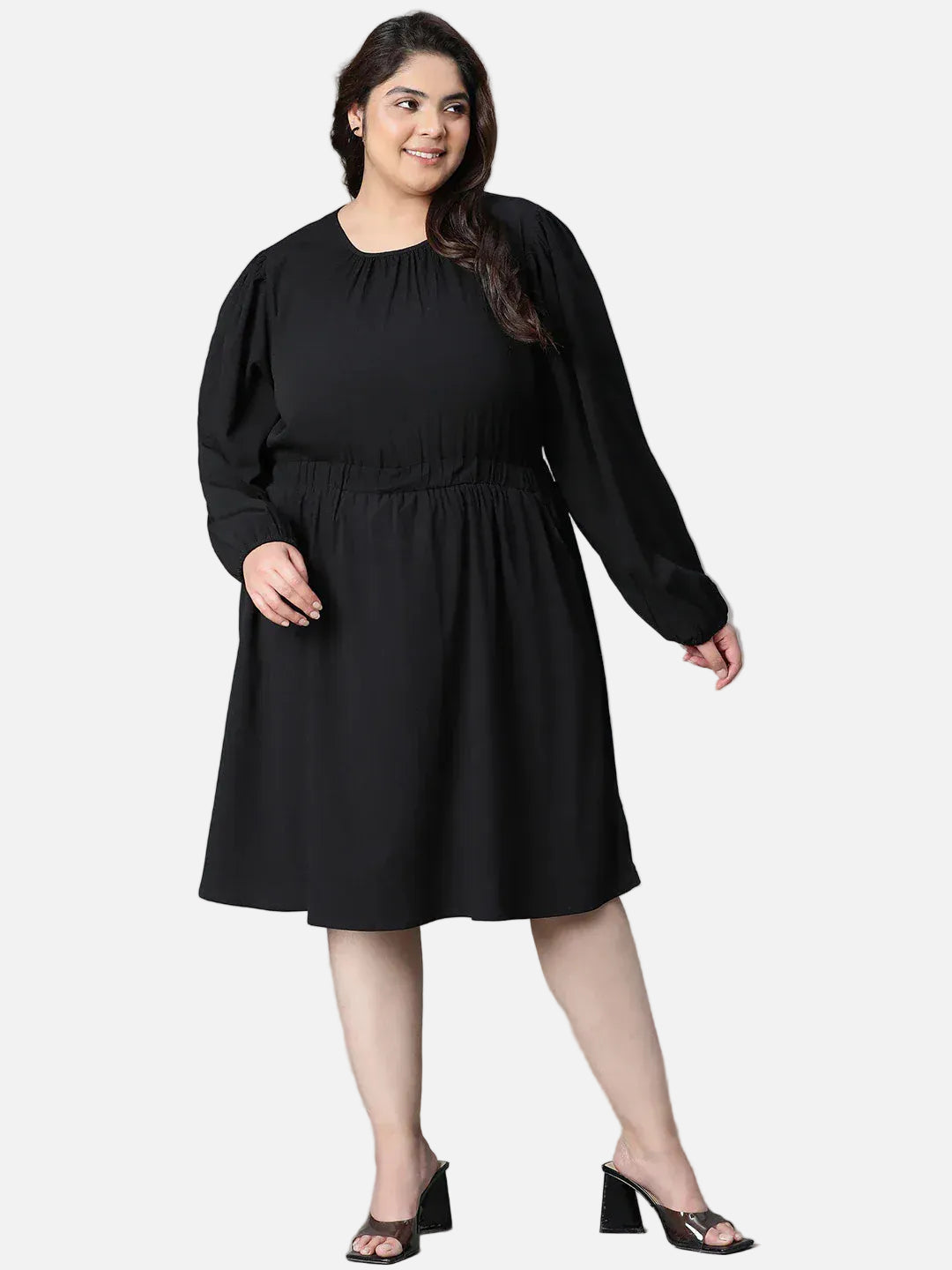 A woman wearing a black dress with long sleeves and a ruched waist, smiling at the camera.