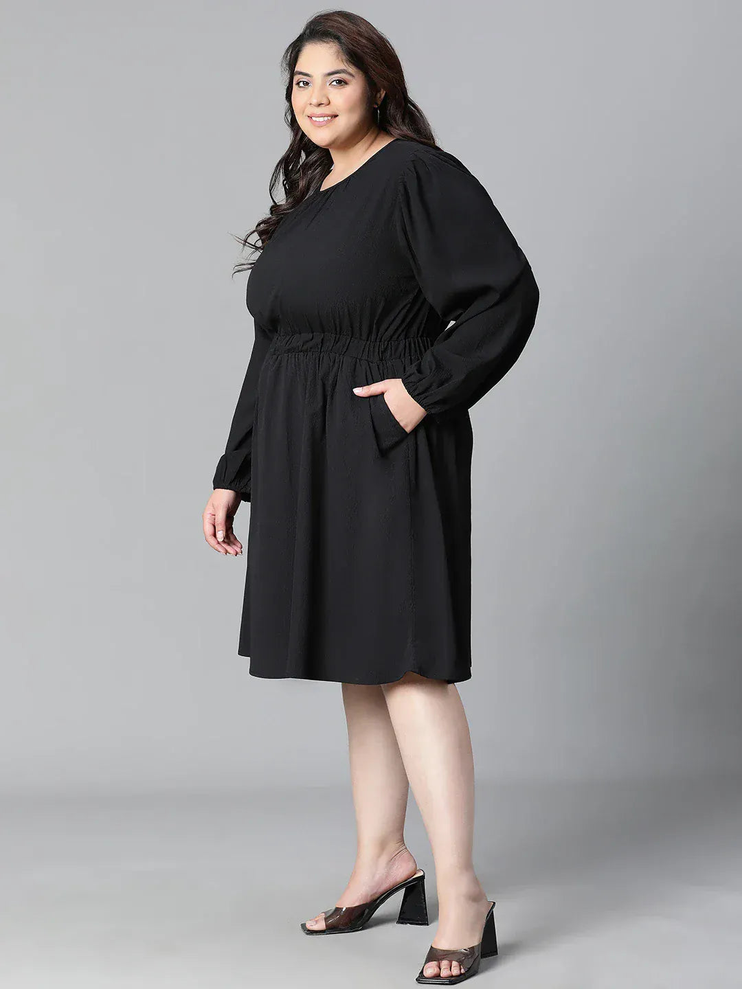 A woman wearing a black dress with long sleeves and a ruched waist, smiling at the camera.