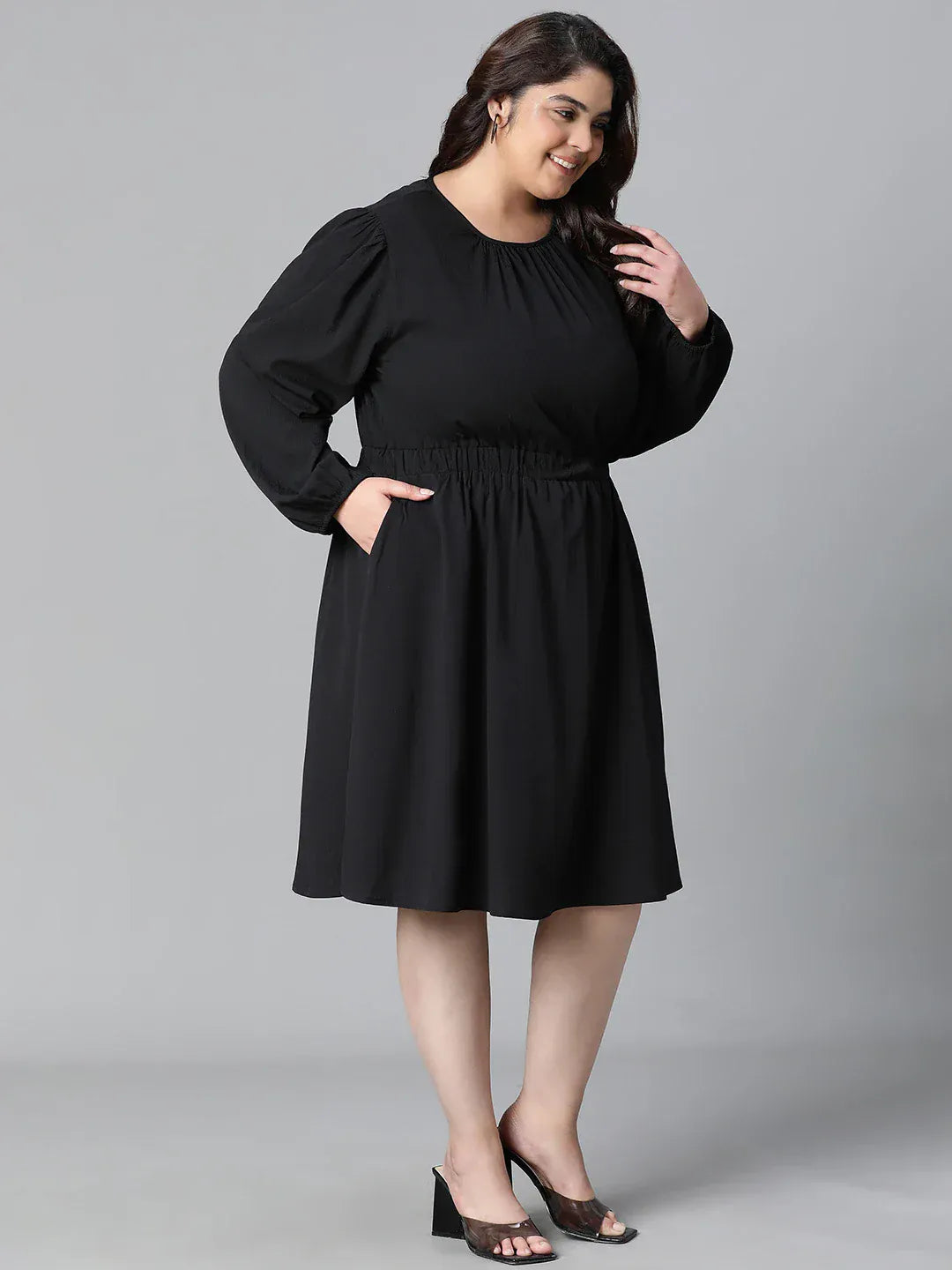 A woman wearing a black dress with long sleeves and a ruched waist, smiling at the camera.