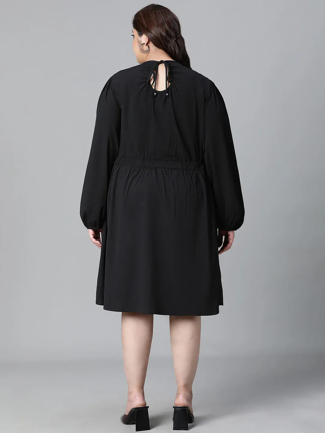 A woman wearing a black dress with long sleeves and a ruched waist, smiling at the camera.