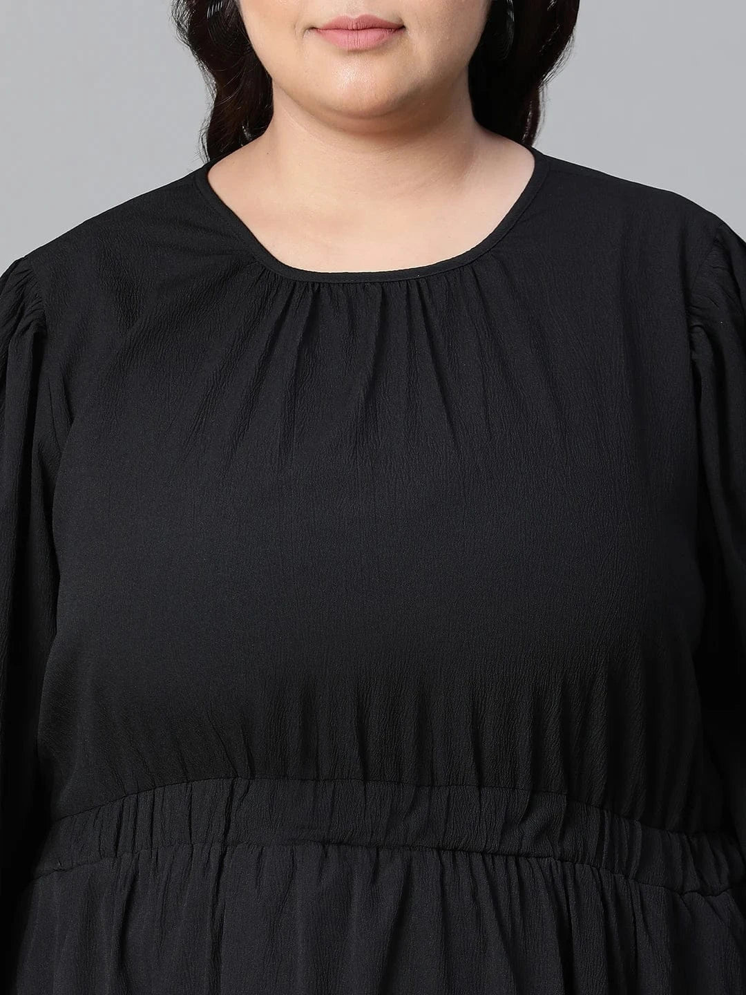 A woman wearing a black dress with long sleeves and a ruched waist, smiling at the camera.