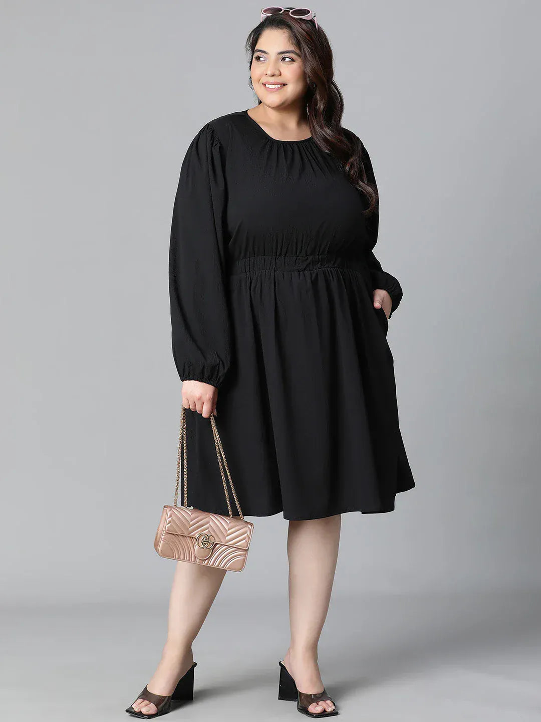 A woman wearing a black dress with long sleeves and a ruched waist, smiling at the camera.