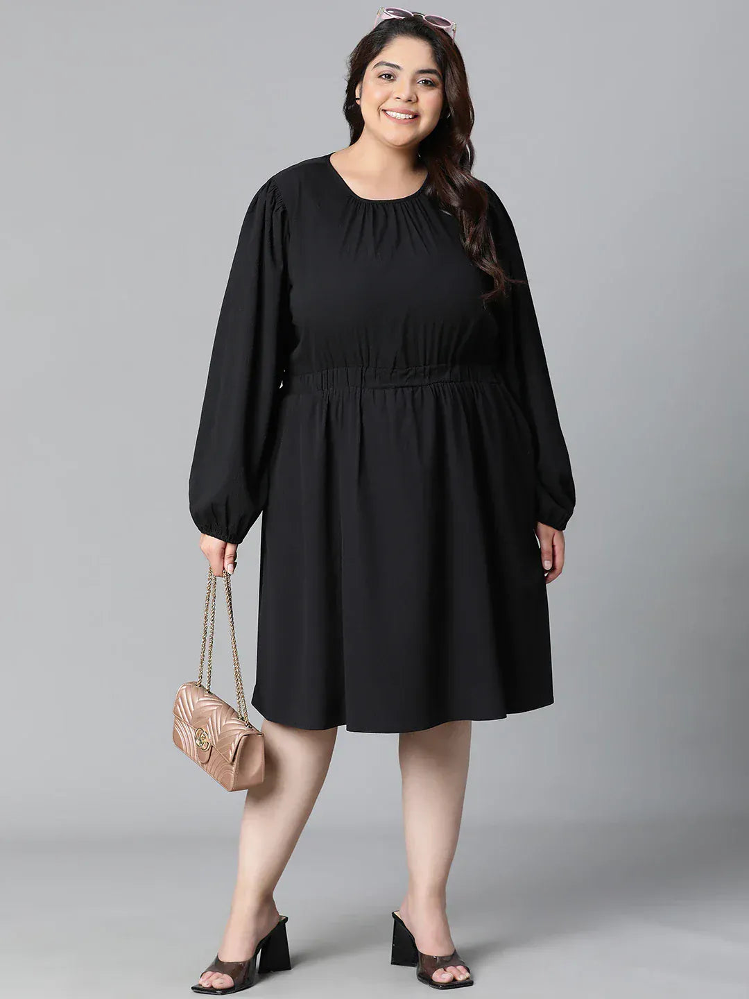 A woman wearing a black dress with long sleeves and a ruched waist, smiling at the camera.