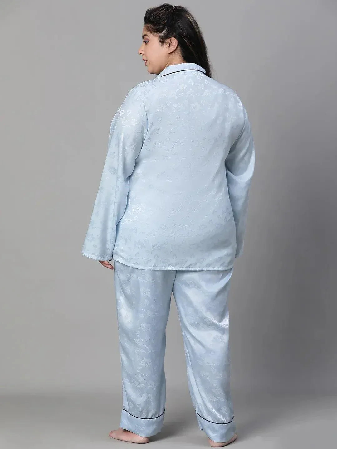 A woman wearing a light blue pajama top and matching pants, standing against a white background.