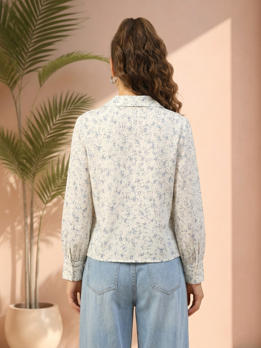 Woman wearing floral print blouse with long sleeves, paired with light blue jeans, back view