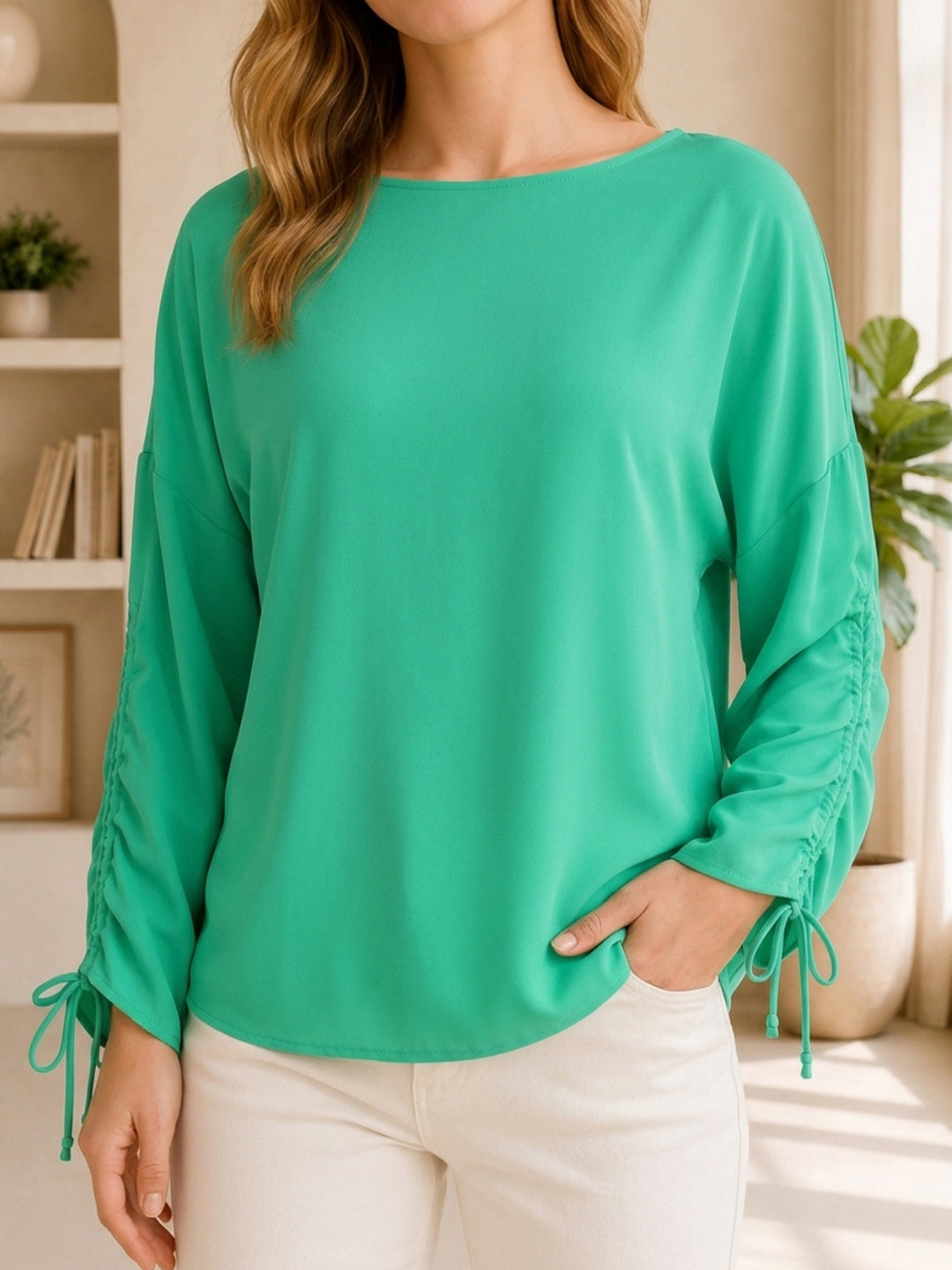Green long sleeve blouse with ruched sleeves and side ties, paired with white pants for casual women's fashion.
