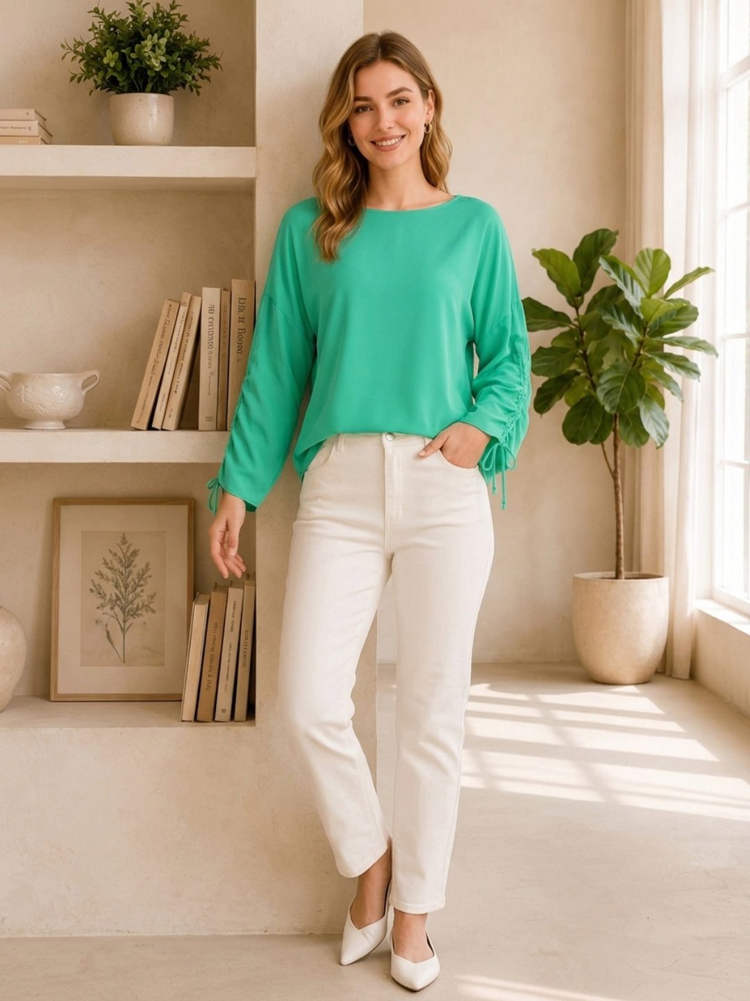 Woman in mint green long sleeve top with tie cuffs, white jeans, and white heels, styled for casual chic fashion.