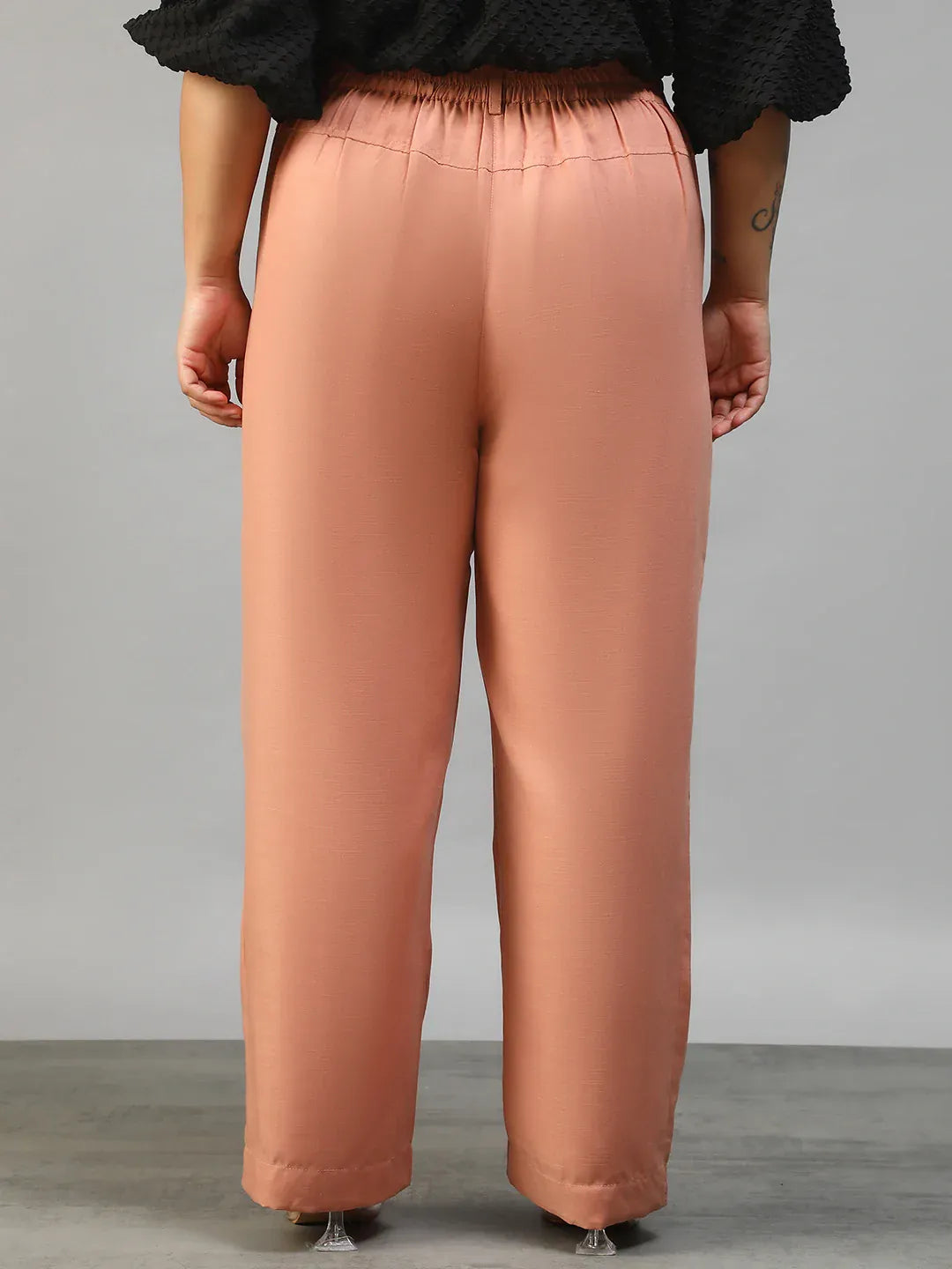 A woman wearing peach-colored wide-leg pants with a high waist and a black top.