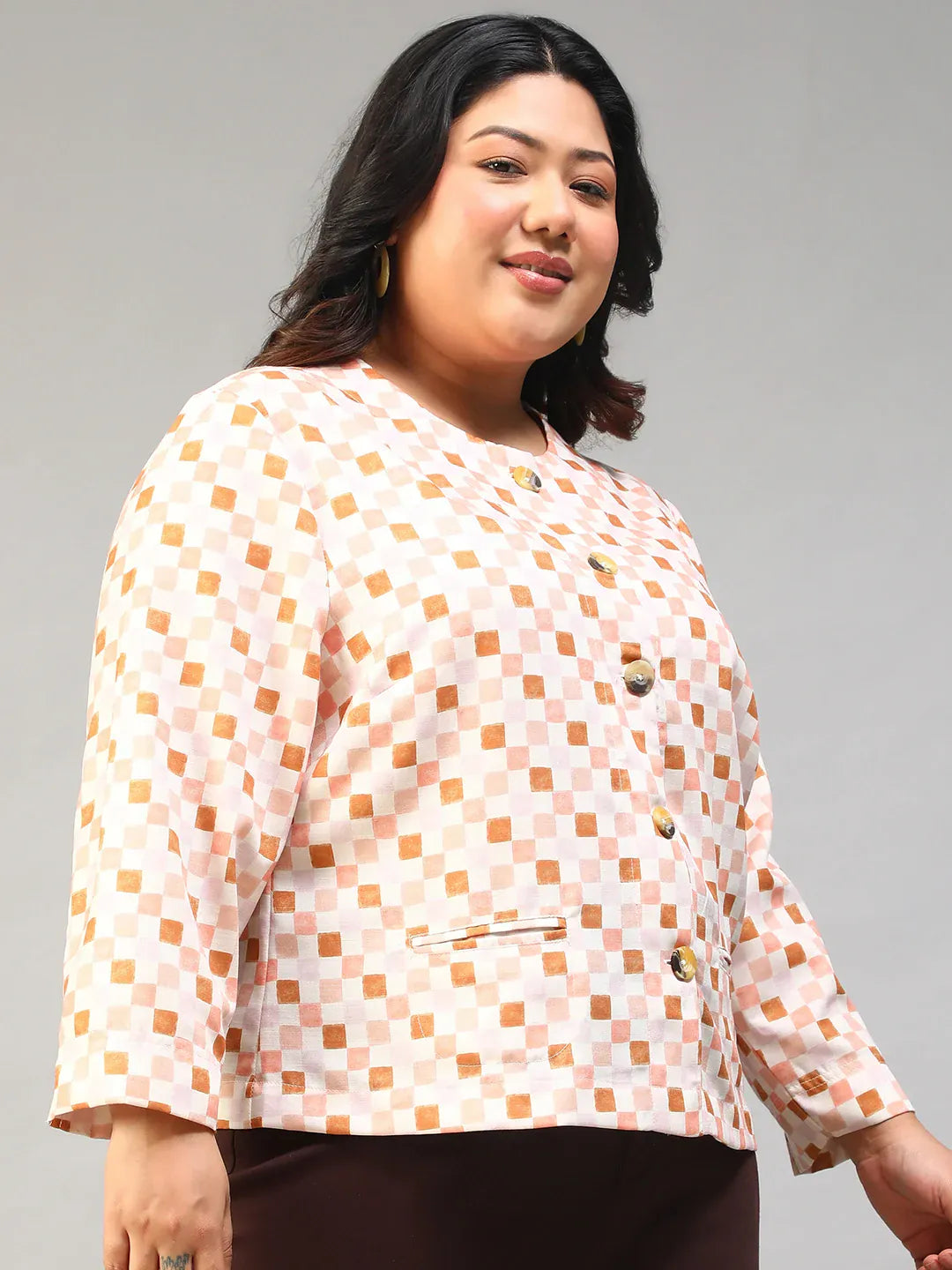 A smiling woman with long dark hair wearing a white and orange checkered jacket with buttons.